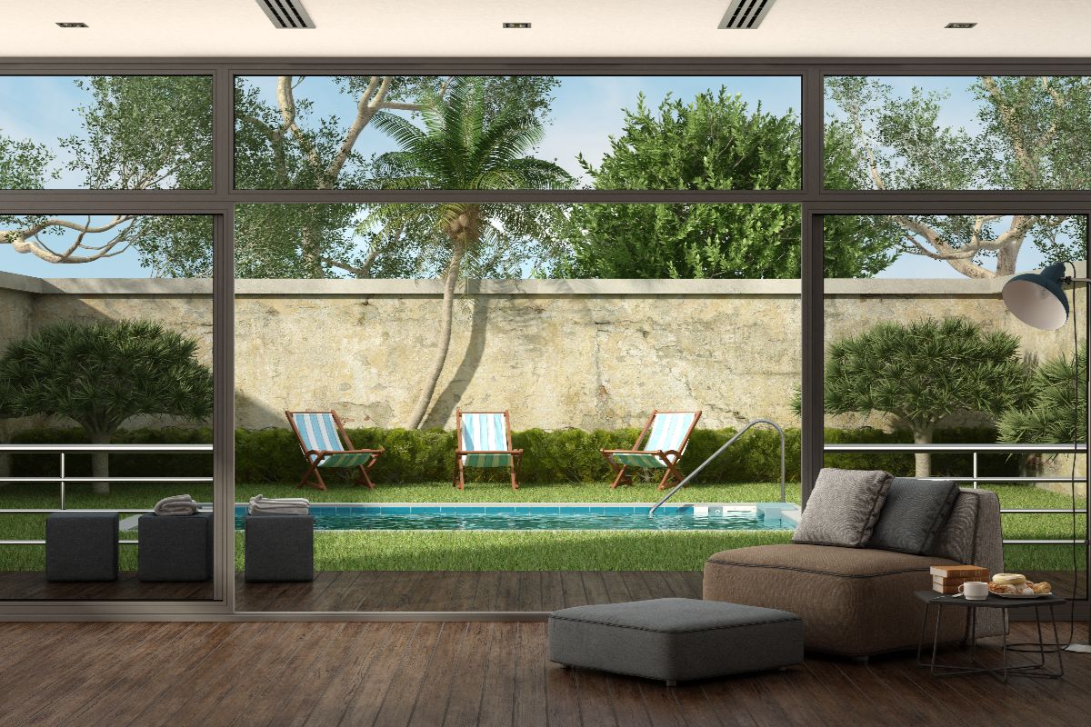 Floor-to-ceiling aluminum glass doors opening from a modern living room to a garden and pool area