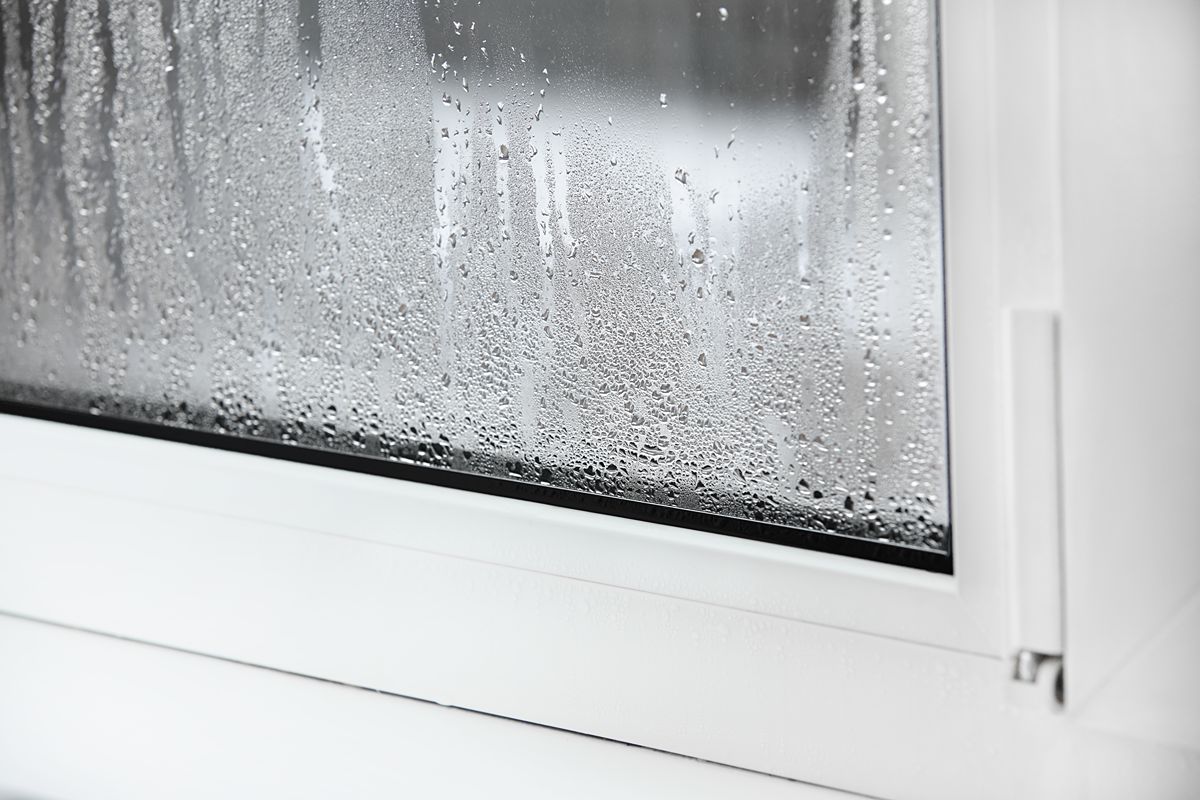 Close-up of rainwater and condensation on a sliding door glass panel with a sealed white frame