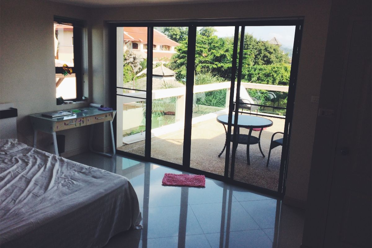 Bedroom with black-framed sliding glass doors opening to a balcony with outdoor seating and greenery