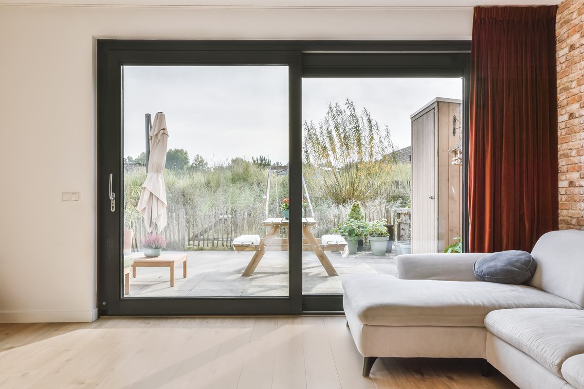 Black aluminum sliding glass door connecting a bright living room to an outdoor patio and garden