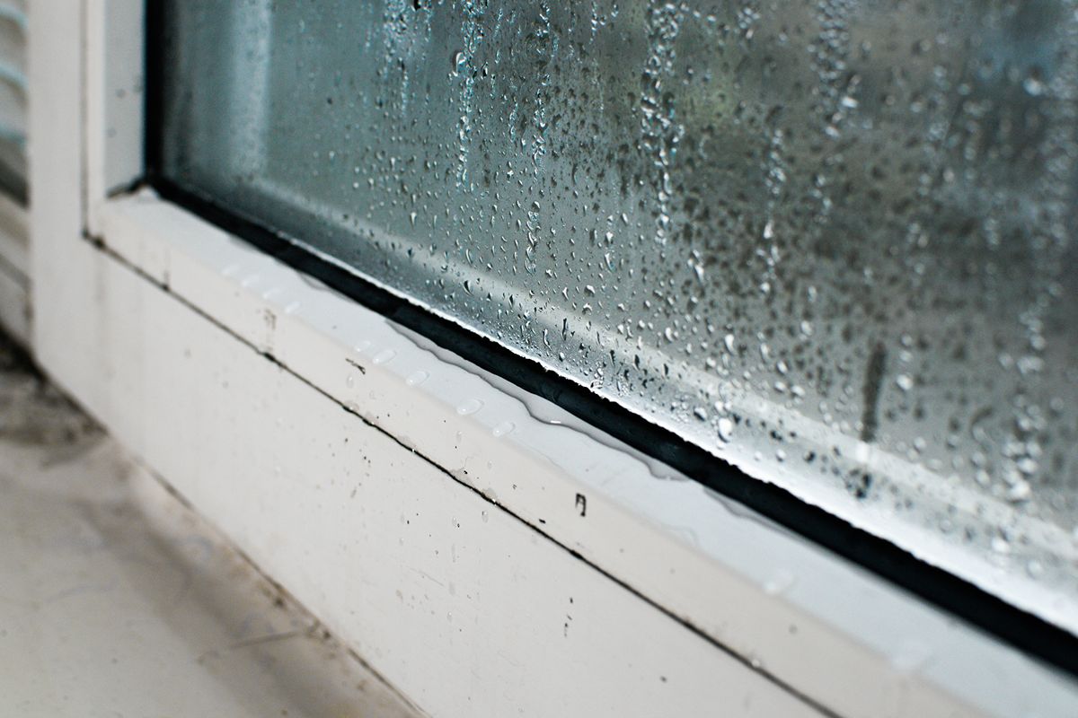 Close-up of rainwater and condensation collecting along the bottom frame of a glass door