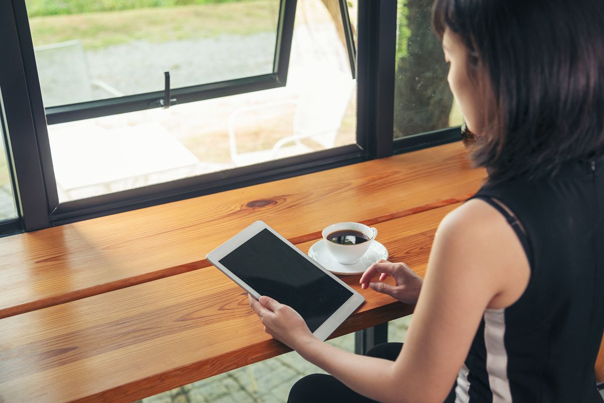 Woman using a tablet beside black aluminum awning windows in a modern interior with a wooden countertop